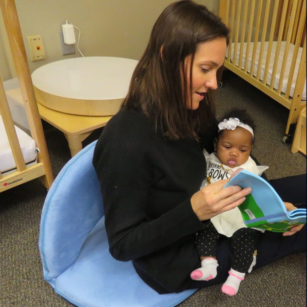 Amanda holding baby while reading to her at NextDoor Milwaukee